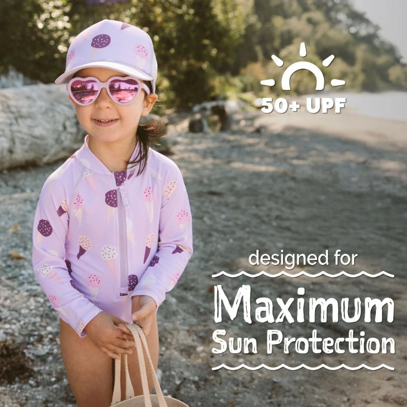 Jan & Jul Girls One Piece UV Swimsuit Lavender Ice Cream on a smiling girl at the beach, showing 50+ UPF.