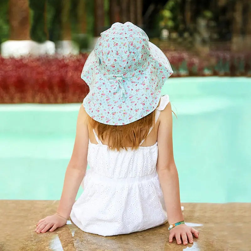 Jan & Jul Kids Cotton Adventure Hat Retro Rose, pale blue floral print, worn by a toddler sitting by a pool.