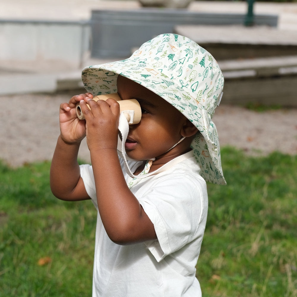 JAN & JUL Kids Cotton Adventure Hat Camp Grove; toddler outdoors wearing white hat with green nature print, peering through a cardboard tube.