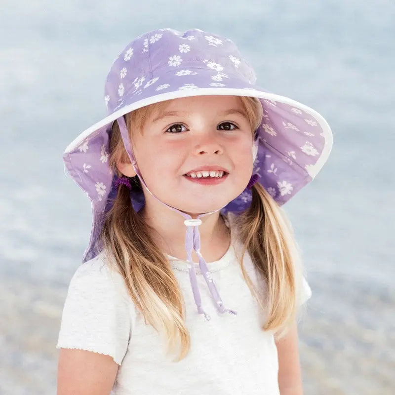 JAN & JUL Kids Cotton Adventure Hats Purple Daisy hat worn by a smiling toddler at the beach with a white brim.