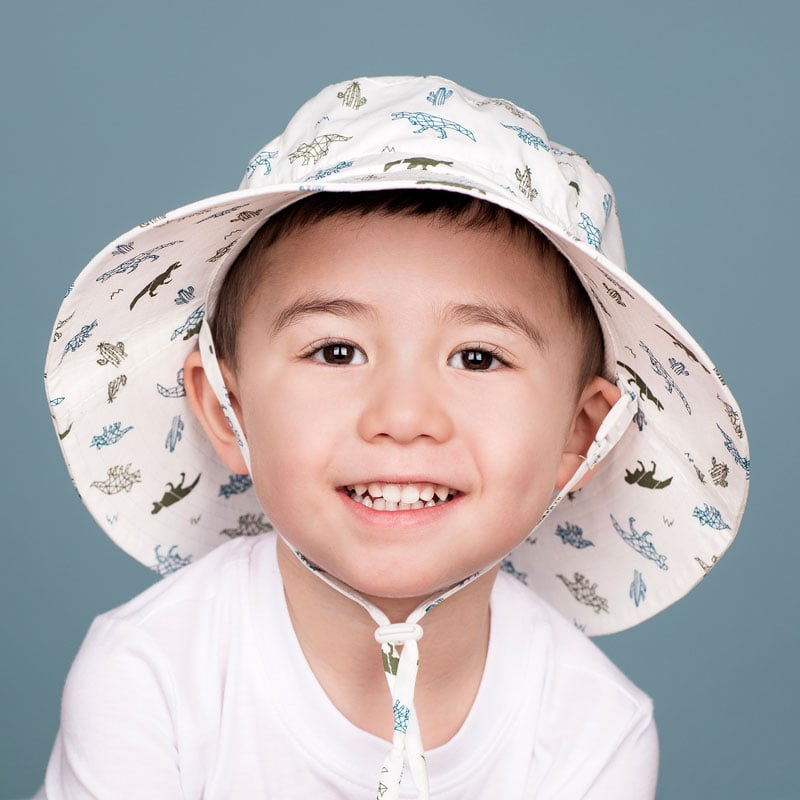 JAN & JUL kids cotton bucket hat with dinosaur print in white, worn by smiling toddler