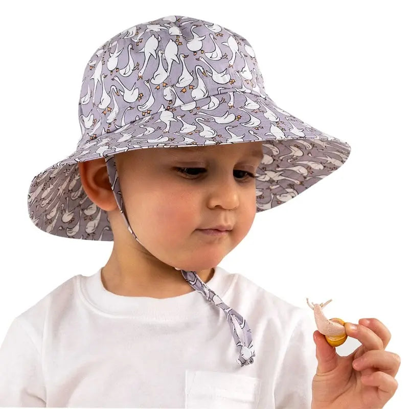 Jan & Jul Kids Cotton Bucket Hat Goose, gray goose print with chin strap, on toddler holding a small toy.