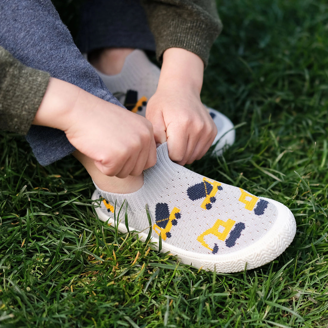 Jan & Jul Kids Graphic Slip-On Shoes - Grey Construction - child pulling on Grey Construction shoes