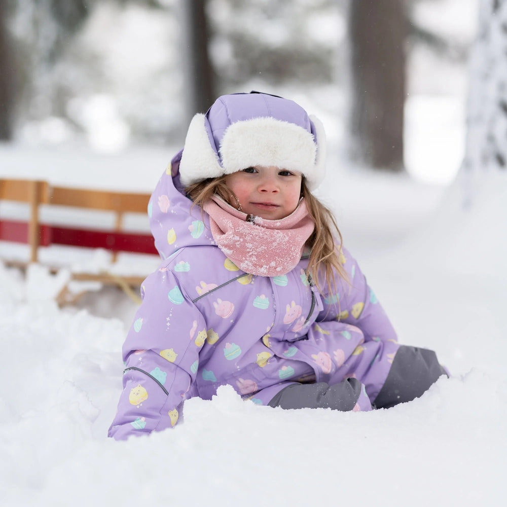 JAN & JUL Kids Insulated Winter Hat Lavender worn by a smiling child in the snow, fluffy earflap warmth.