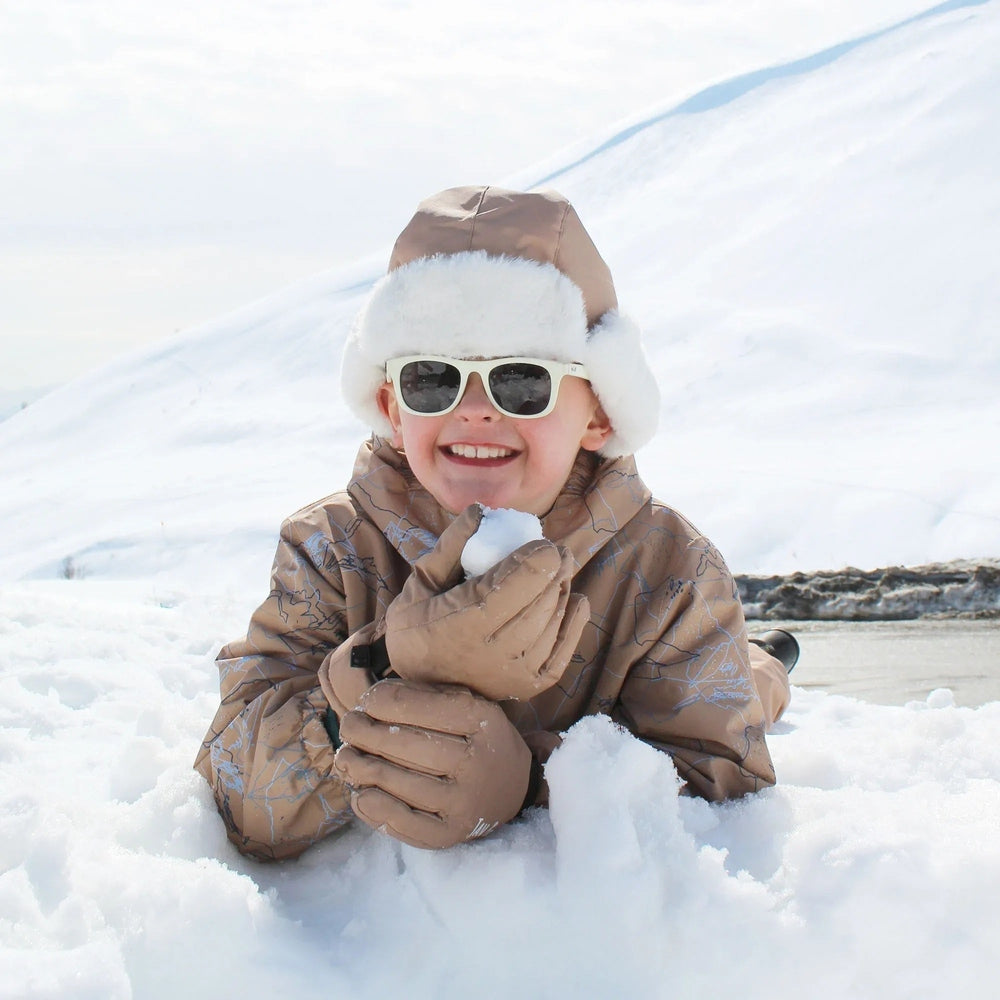 Jan & Jul Kids Insulated Winter Hats Soft Brown with white fur trim, worn by a smiling child playing in the snow.