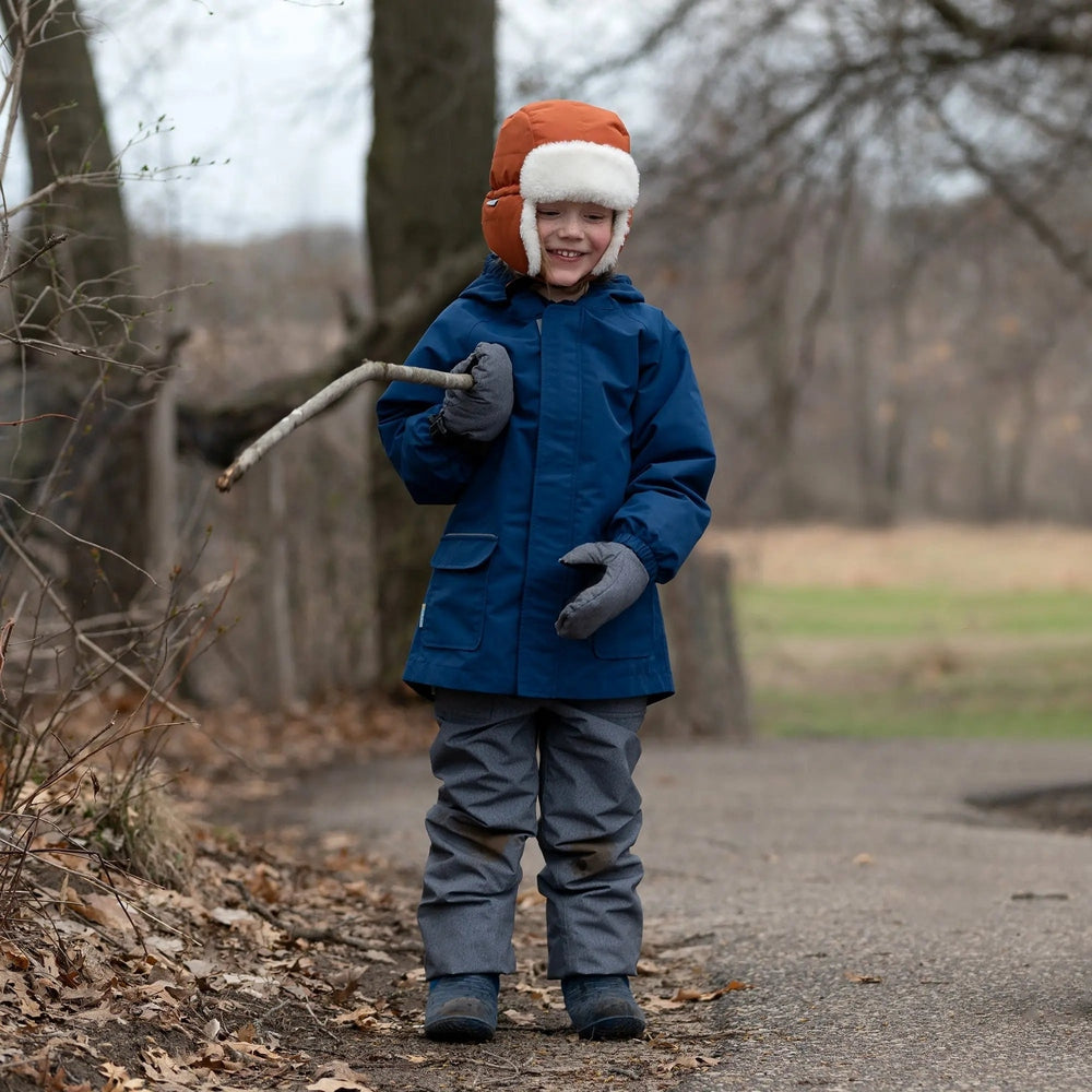 JAN & JUL Kids Insulated Winter Hats Terracotta keeps a smiling child warm outdoors in an orange earflap hat.