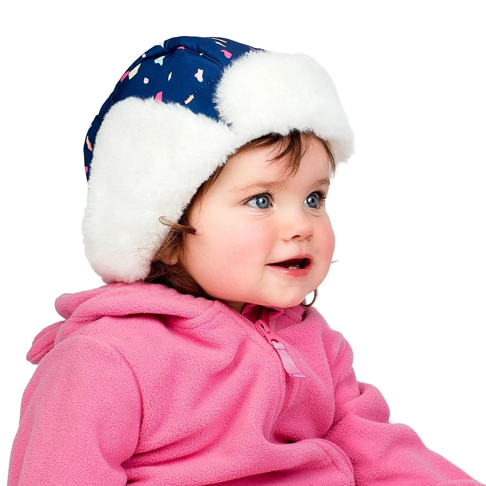 Jan & Jul Kids Insulated Winter Hats Terrazzo blue with white faux fur trim worn by a smiling toddler in pink fleece.