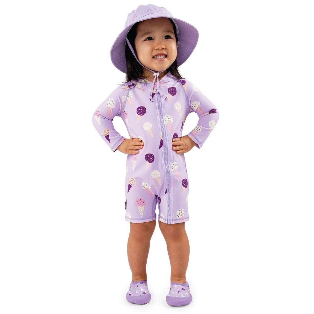 JAN & JUL lavender ice cream UV sun suit on a smiling toddler, zipper front, standing with hands on hips.