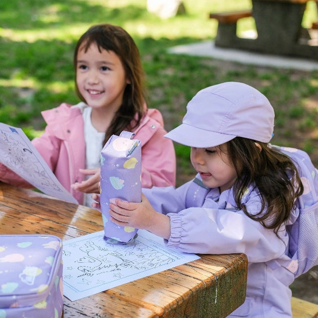 JAN & JUL Kids Pencil Case Macarons in lavender pastel print, on a wooden picnic table