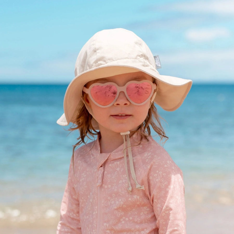 JAN & JUL Frosty Lavender polarized heart sunglasses with pink frames on a child at the beach