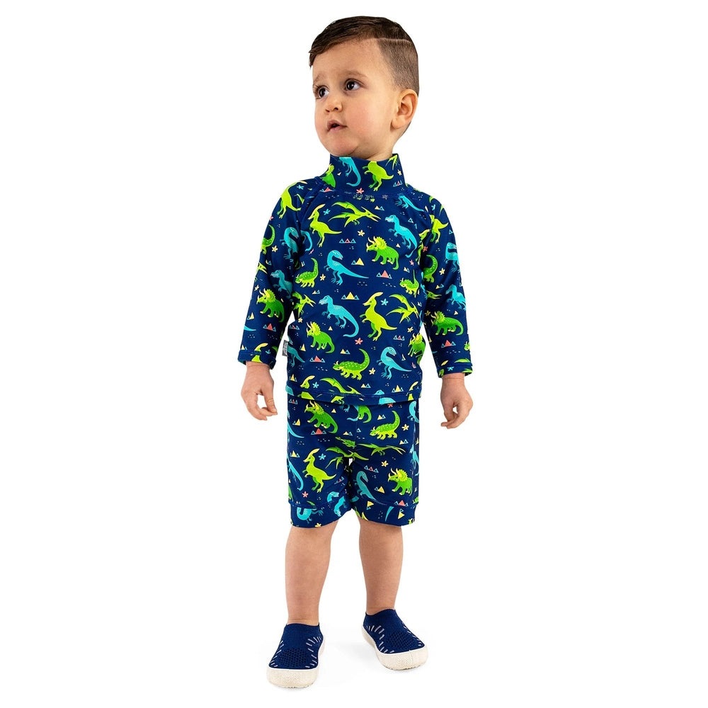 Jan & Jul Dinoland UV rashguard set for kids, navy with neon dinosaurs; toddler stands in matching long-sleeve top and shorts.