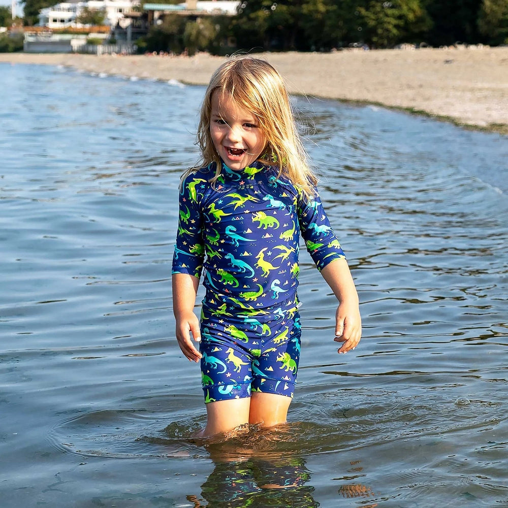 JAN & JUL Jan & Jul Kids UV Rashguard Set Dinoland in navy blue with colorful dinosaurs; child wading in shallow water.