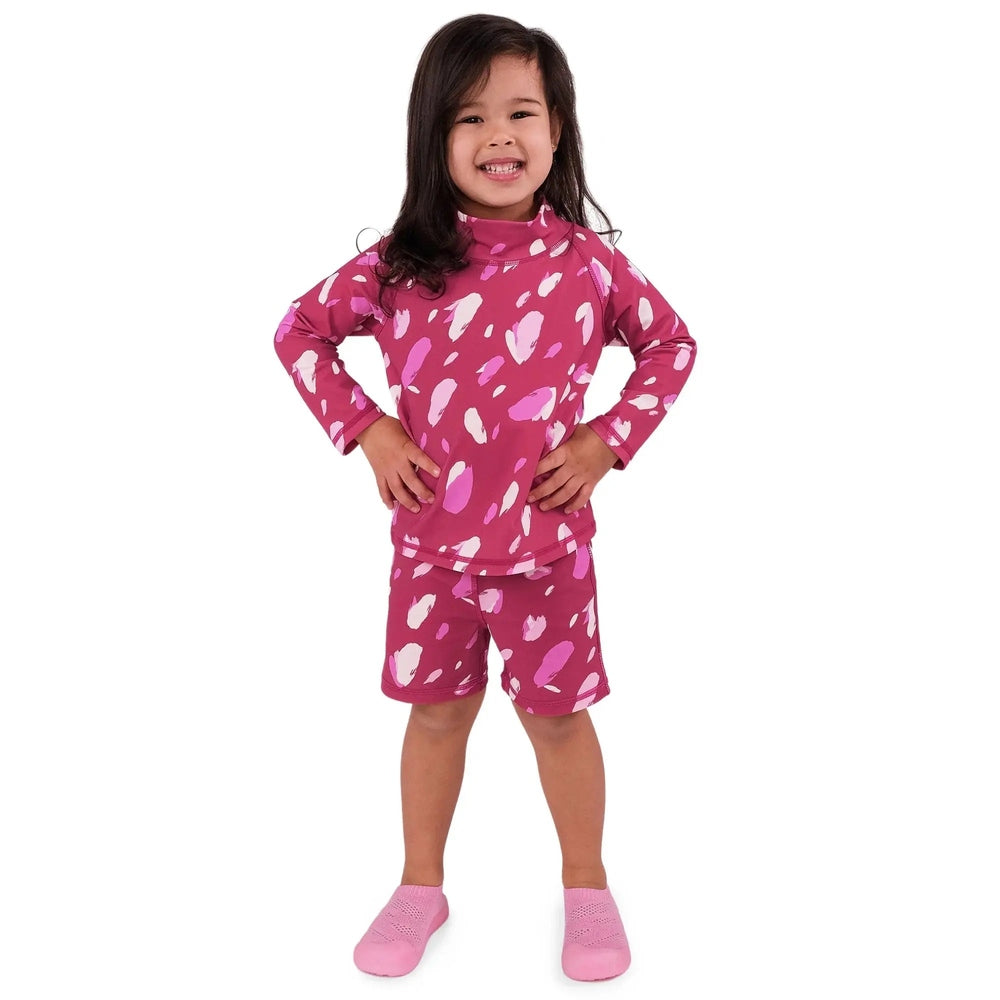 Jan & Jul Kids UV Rashguard Set Pink Petals: smiling toddler stands with hands on hips in pink petal-print long-sleeve top and shorts.