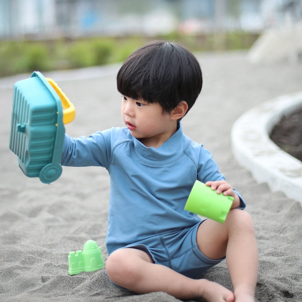 Jan & Jul Kids UV Rashguard Top Blue Grey; toddler plays in sand, holding a green cup and teal toy.