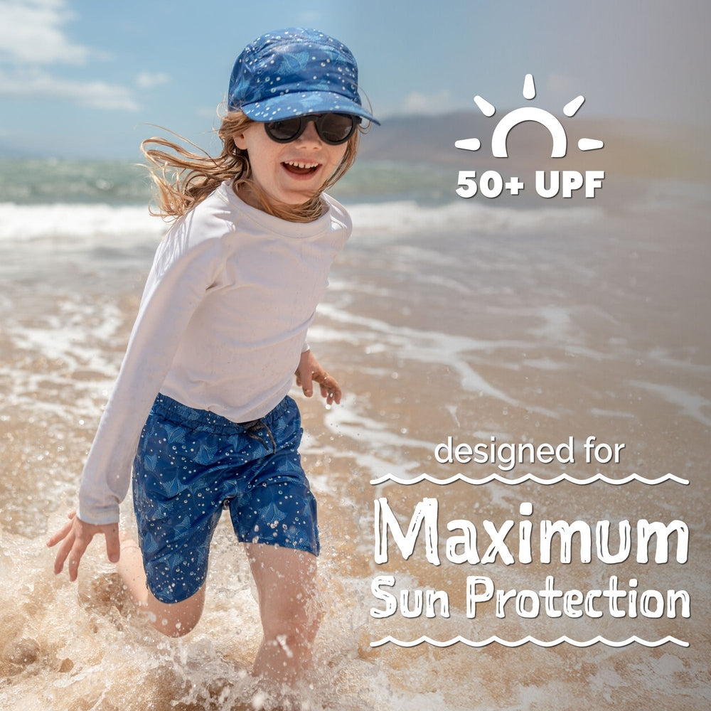 JAN & JUL Kids UV Swim Shorts Manta Ray, blue manta-ray print; child runs along the beach splashing water, 50+ UPF