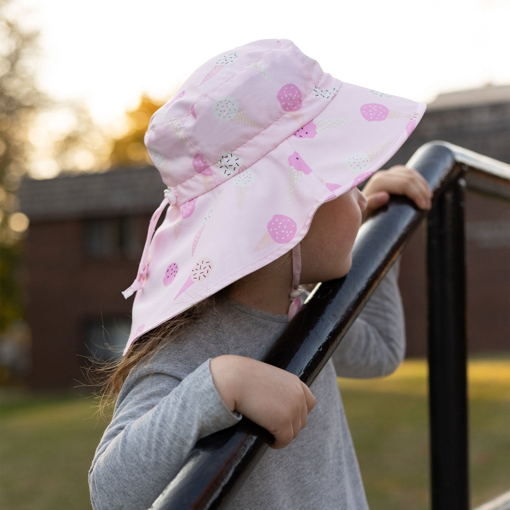 Jan & Jul Kids Water Repellent Adventure Hat Pink Ice Cream pattern; a child grips a railing outdoors, sunny and playful.