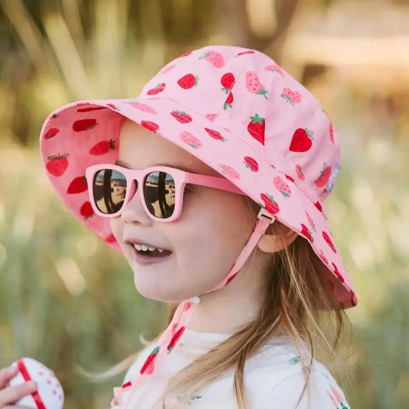 JAN & JUL Kids Water-Repellent Bucket Hat Pink Strawberry, girl outdoors wearing hat with chin strap fastened.
