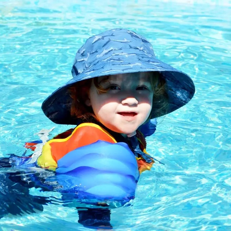 Jan & Jul Kids Water Repellent Shark Bucket Hat on a toddler swimming in a bright blue pool.