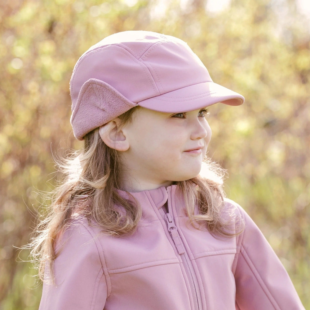 Jan & Jul Kids Water Resistant Softshell Cap Dusty Rose; girl outdoors wearing dusty rose cap with ear flaps.