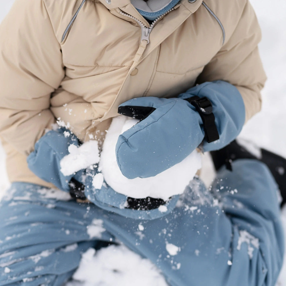 JAN & JUL Kids Waterproof Mittens Dusty Blue; child outdoors in snow, cupping snow with blue mittens.