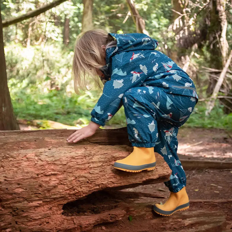 Jan & Jul Puddle Dry Rain Boots With Handle Yellow on a toddler climbing a log outdoors in a blue patterned outfit.