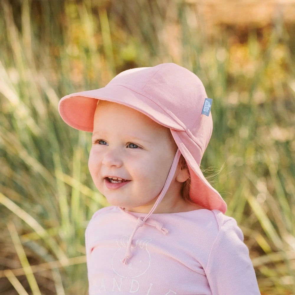 Jan & Jul Sun Soft Baby Cap Rose Quartz worn by a smiling toddler in a pink brimmed sun hat outdoors.