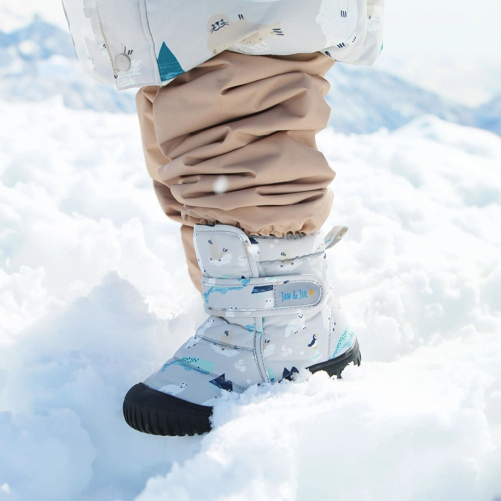 Jan & Jul Toasty Dry Booties Polar Pals baby snow boots in light gray with blue pattern, Velcro straps shown as they step through snow.