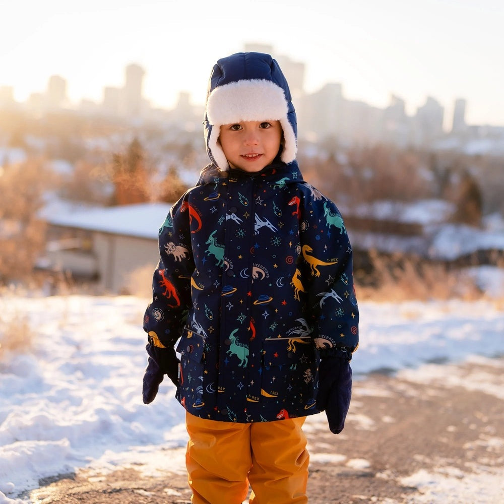 Jan & Jul Space Dinos Rain Jacket, navy with fleece-lined hood, worn by a child standing in a snowy park.