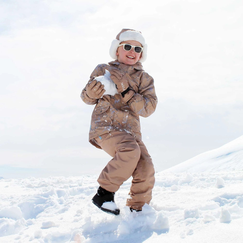 Jan & Jul Waterproof Cozy Dry Rain Pants in soft brown, worn by a smiling child playing in the snow.