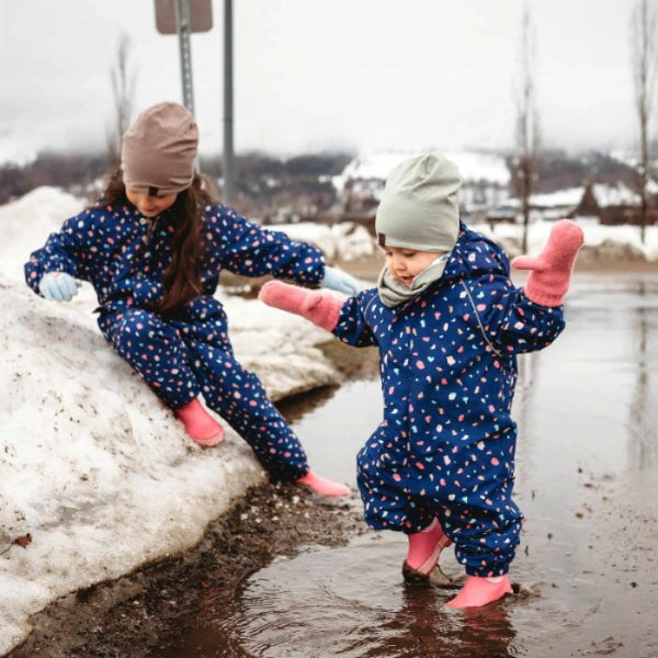 Two toddlers in JAN & JUL Waterproof Cozy Dry Rain Suit Terrazzo, blue with pink mittens, splashing in a puddle.