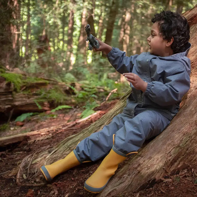 Jan & Jul Waterproof Puddle Dry Rain Pants for kids in heather grey, worn by a child sliding down a log in a forest.