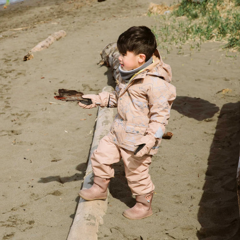 Jan & Jul waterproof puddle-dry rain pants in soft brown worn by a child walking along a sandy beach in boots