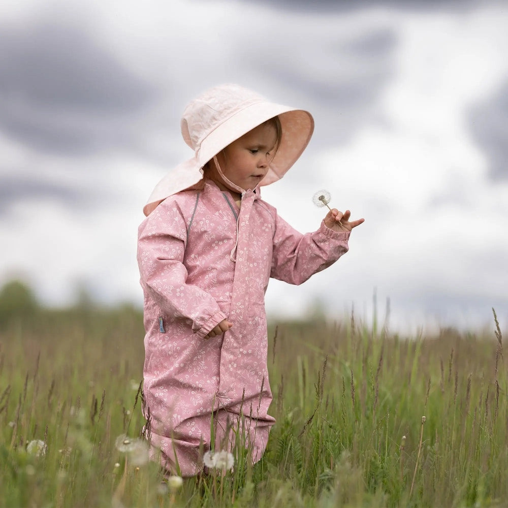 Jan & Jul Waterproof Puddle Dry Rain Suit Prairie Flowers; a child in pink floral rain suit stands in tall grass blowing a dandelion.