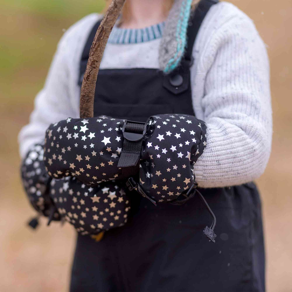 Toddler wearing JAN & JUL Waterproof Toasty Dry Mitten Black Star mittens gripping a twig outdoors