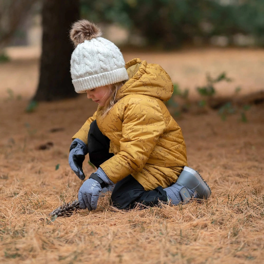 JAN & JUL Toasty-Dry waterproof snow gloves Wildberry worn by a child outdoors, kneeling to pick up a pine cone.