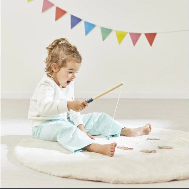 Child playing with fishing rod on a white floor with colorful flags hanging above.