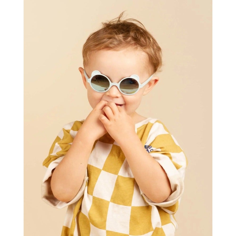 Ki Et La Sunglasses Ourson Sky Blue, round white-framed shades worn by a smiling toddler.