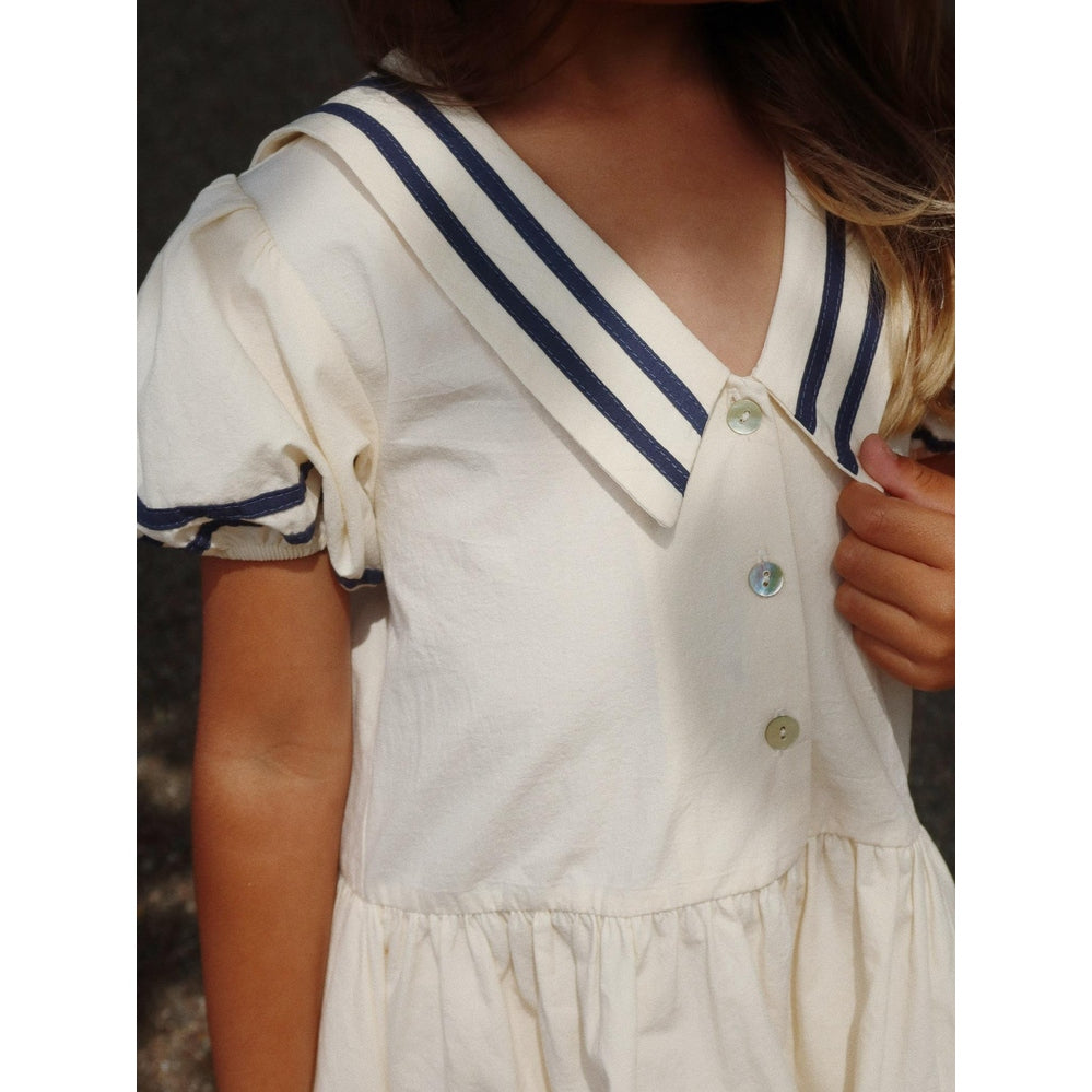 Konges Sløjd Allie Sailor Dress optic white with navy striped collar and puff sleeves, girl gently adjusting the collar.