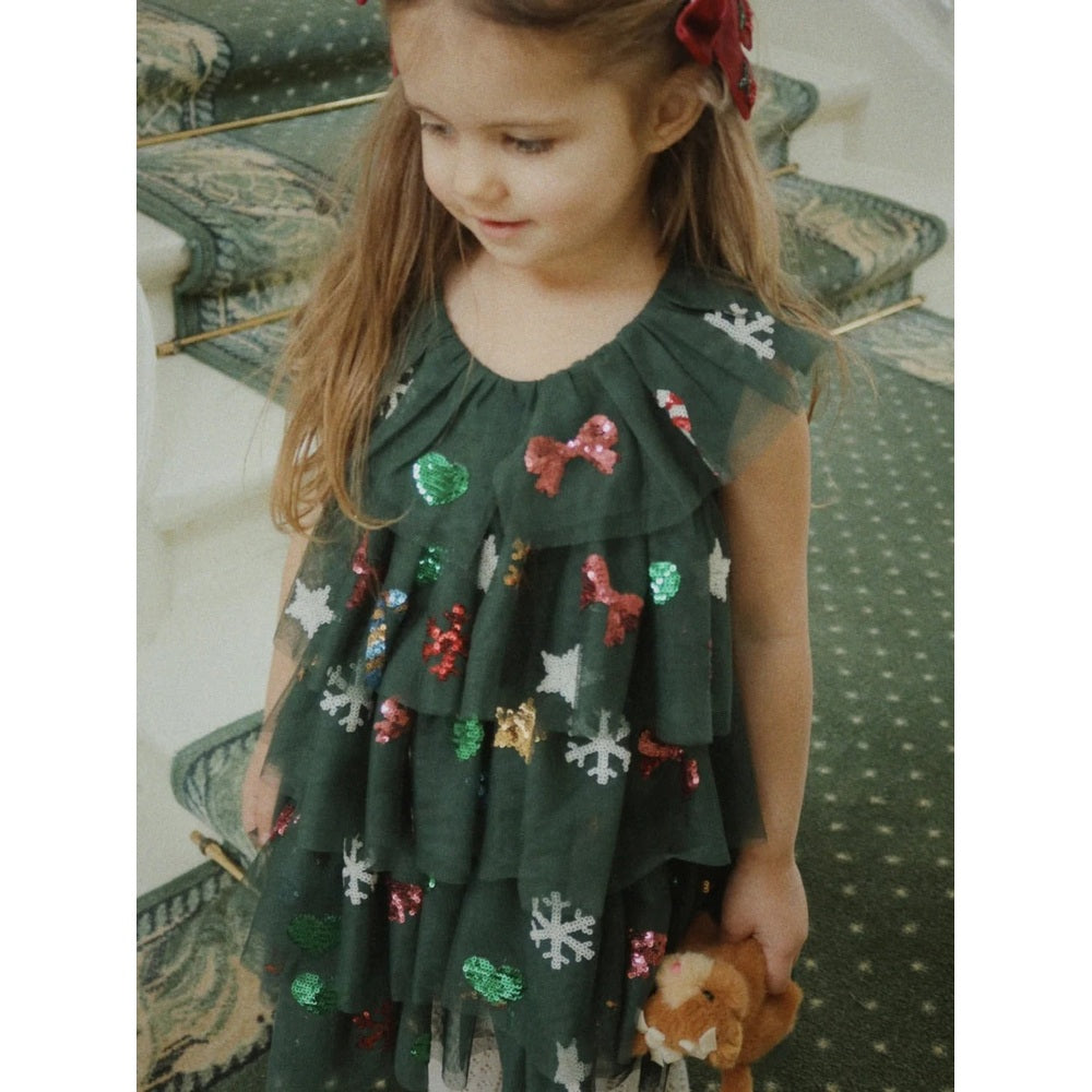 Konges Slojd Baby Animals plush toy held by a young girl in a dark green sequined dress, festive mood