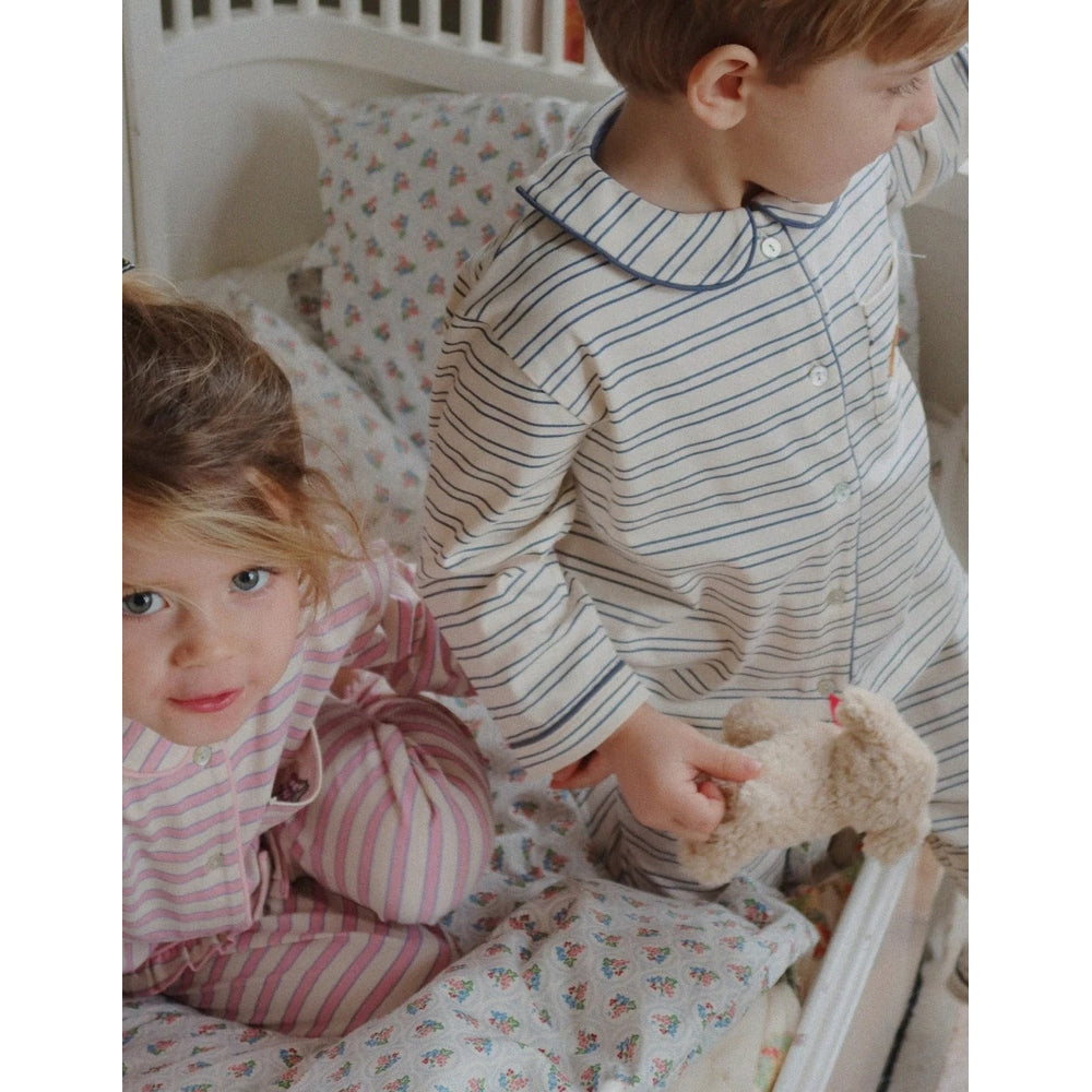 Konges Slojd Baby Animals plush toy; fluffy cream bear handed to a child as two kids sit in striped pajamas.