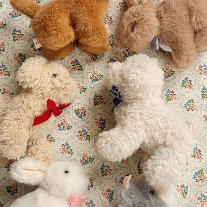 Konges Slojd Baby Animals plush toys in cream, brown, and gray with bows on a floral quilt.