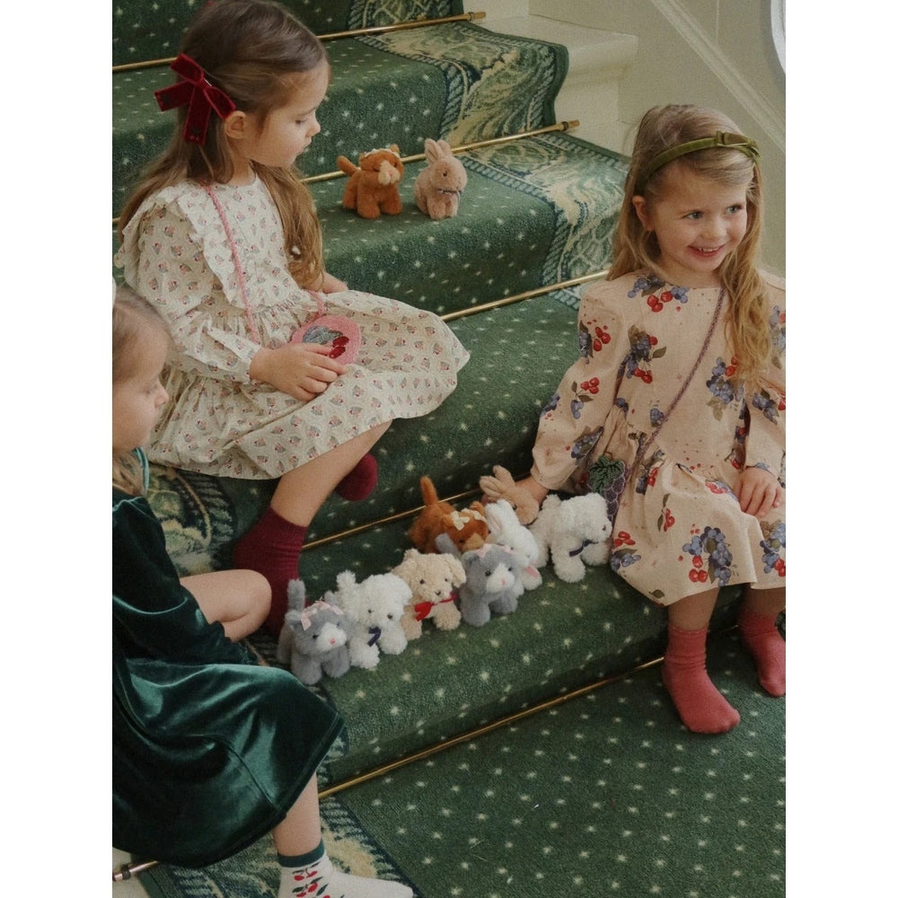 Konges Slojd Baby Animals plush toys lined along green-carpeted stairs as two girls play nearby.