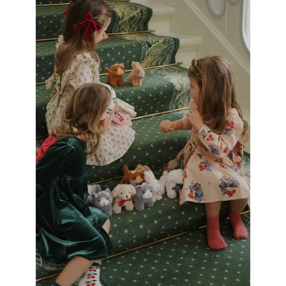 Konges Slojd Baby Animals plush toys lined up on a green-carpet staircase as three kids play nearby.