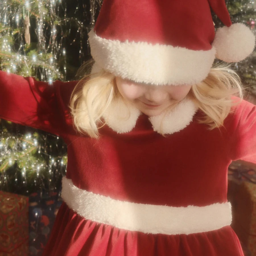 Konges Slojd Christmas Dress Red Dahlia: red velvet dress with white faux‑fur trim, worn by a child with arms outstretched.