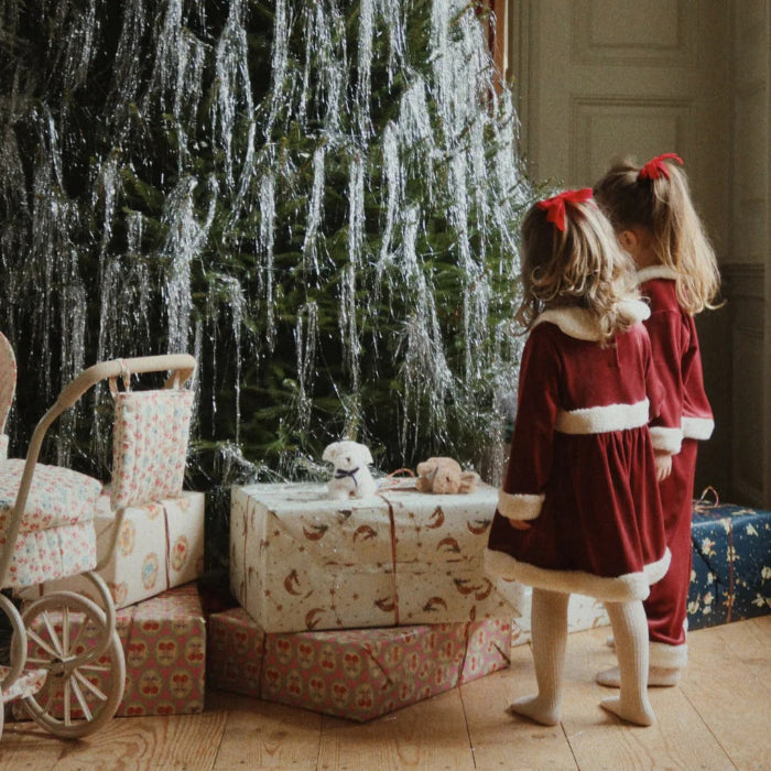 Konges Slojd Christmas Set Red Dahlia toddler outfits; two girls wear red velvet coats with white fur trim beside wrapped gifts.