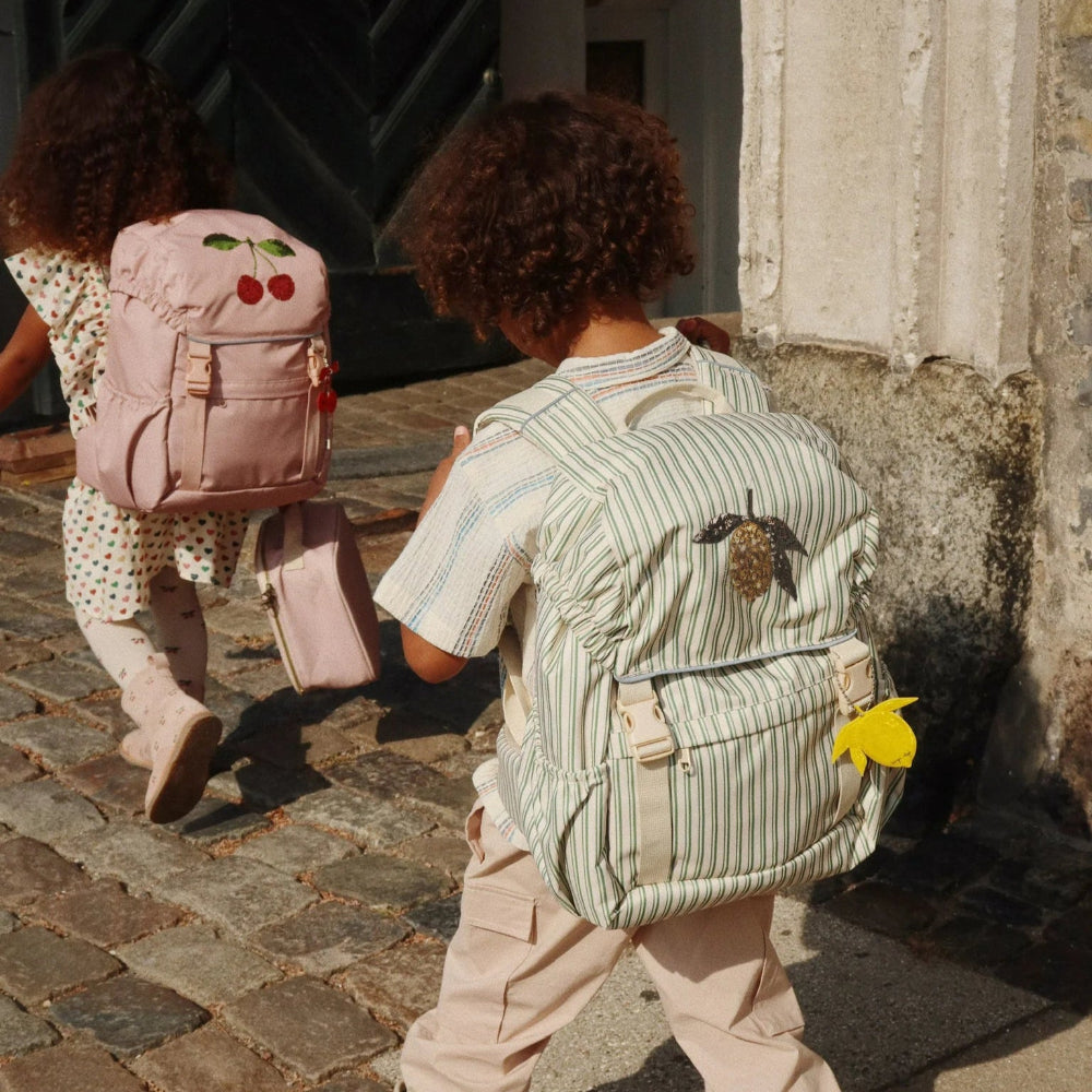Konges Slojd Clover schoolbags; two backpacks, one green striped with a yellow leaf charm and one pink cherry-embellished.