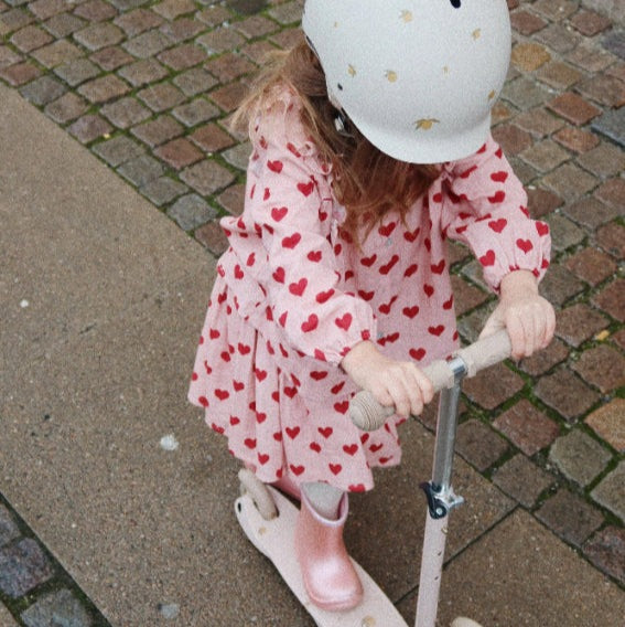 Konges Slojd Coco Skirt GOTS Amour Mellow pink heart-print skirt, toddler riding a scooter outdoors.