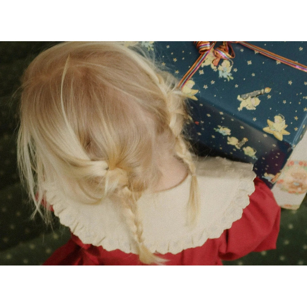 Konges Slojd Coeur Dress Red Dahlia on a toddler, white scalloped collar, braided blonde hair, holding a gift box.