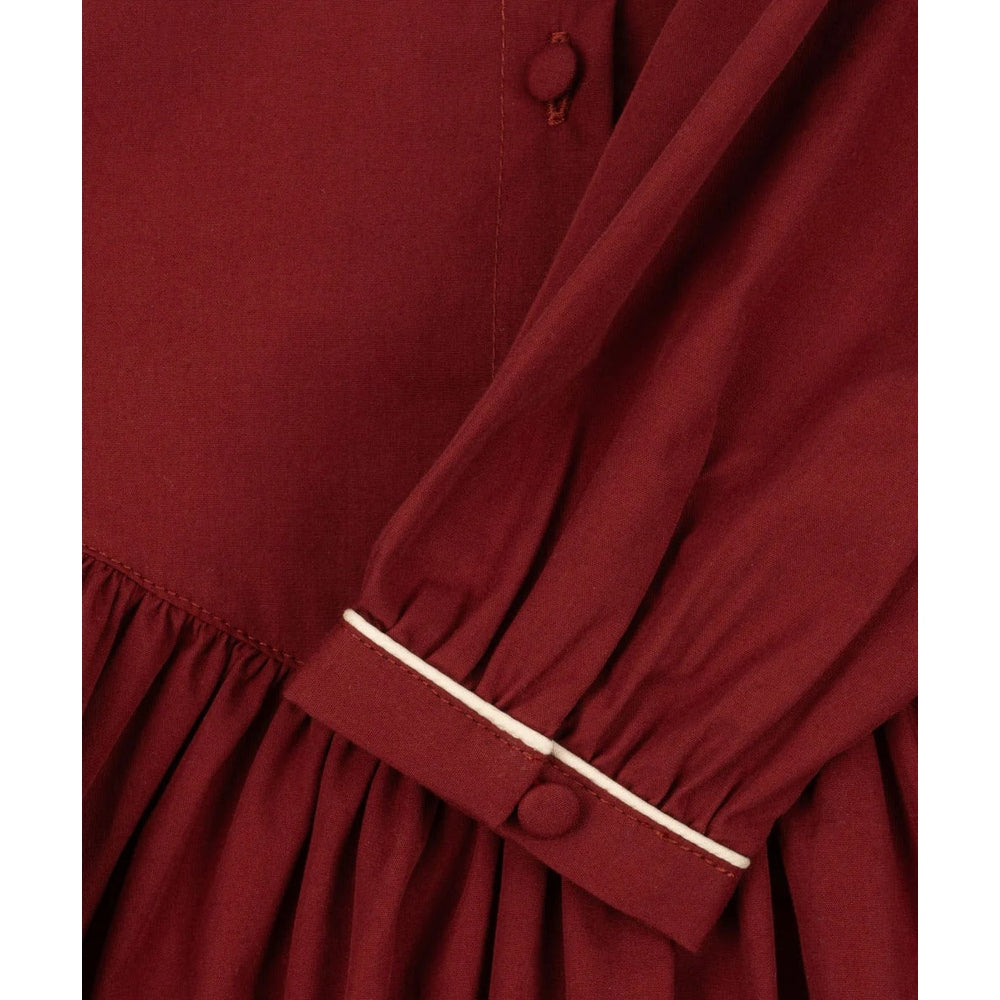 Konges Slojd Coeur Dress Red Dahlia; burgundy baby dress with white piping on the cuff and a gathered skirt.