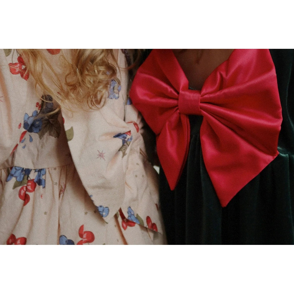 Konges Slojd Gia Bow Dress Pine Grove, cream floral dress beside a black dress with a large red bow.